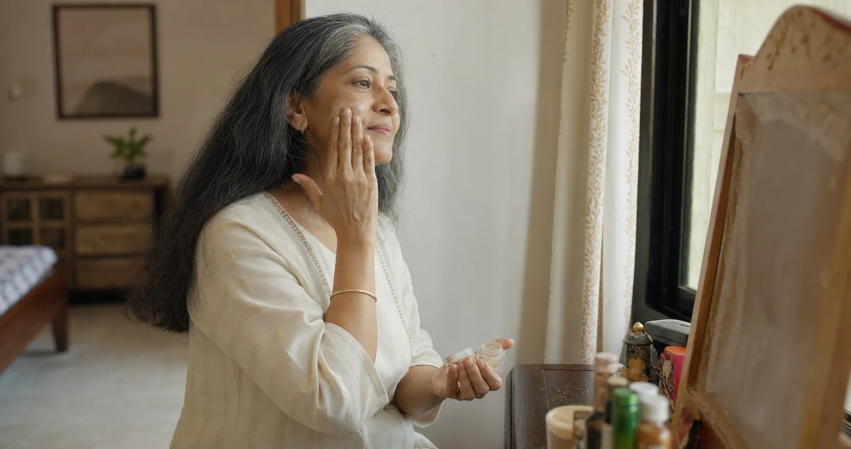 Mature Indian woman applying moisturiser during a calm morning routine