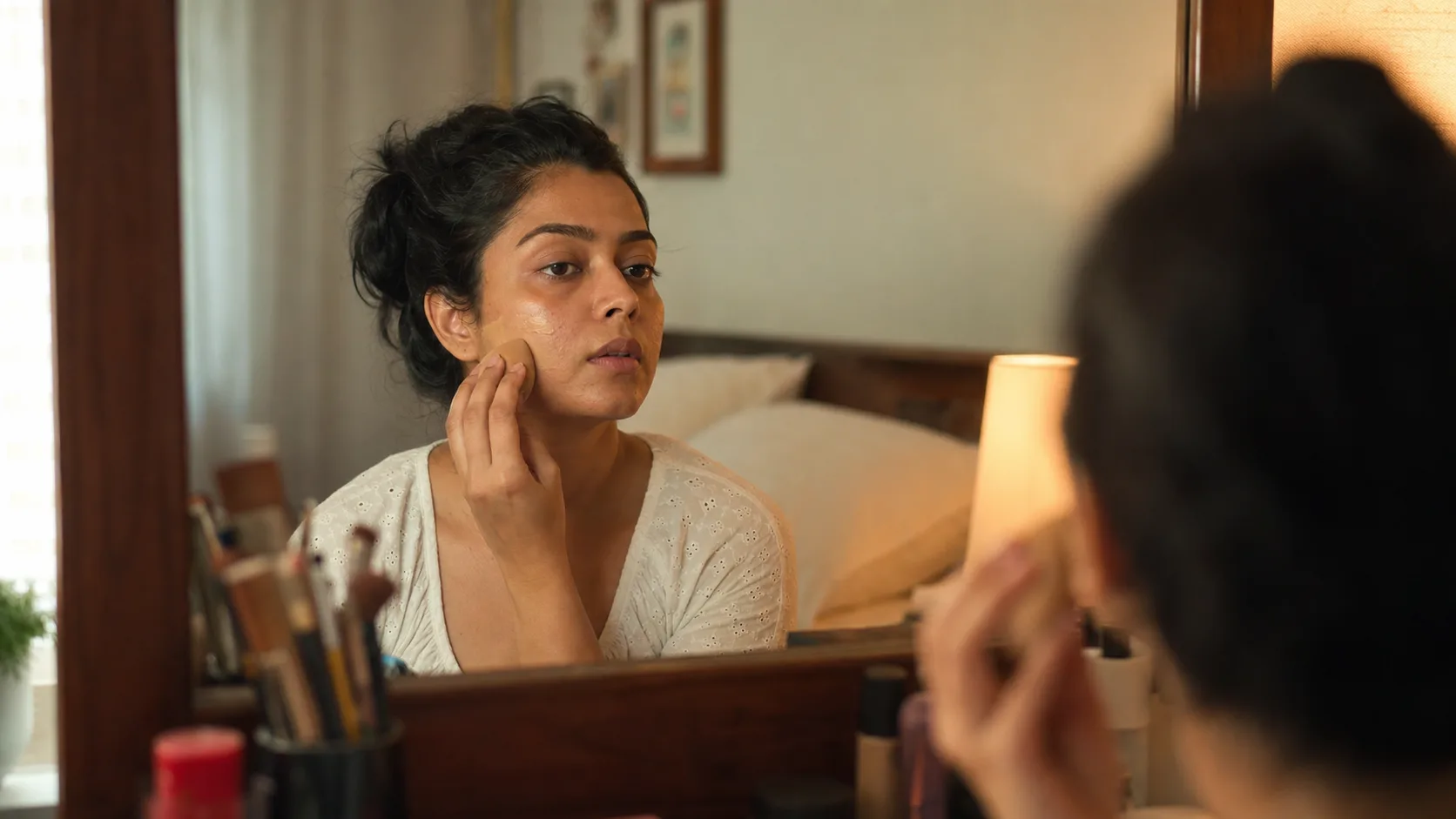 Indian woman applying light base makeup to natural textured skin at home
