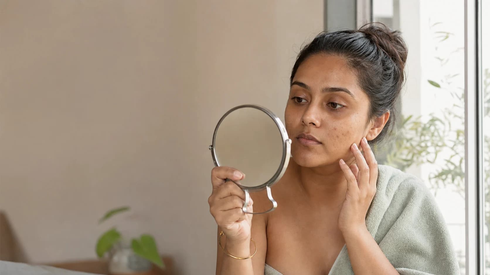Indian woman checking natural skin texture and post-acne marks in soft window light